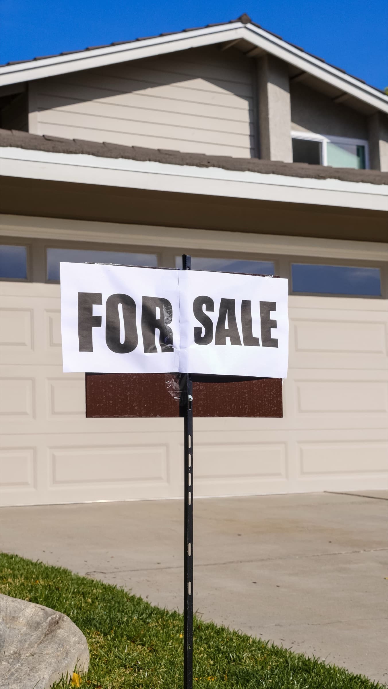 A red and white For Sale yard sign planted in the front lawn of a suburban house