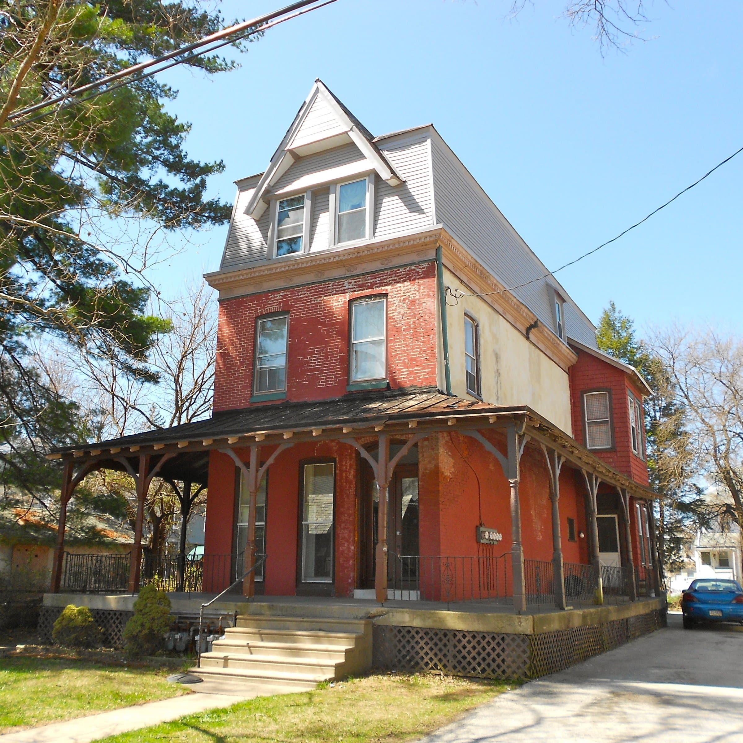 A red-brick Victorian home with a wraparound porch in East Lansdowne